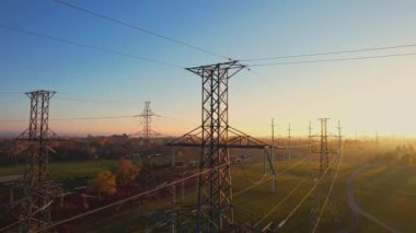 Altın saatinde kablolu iletişim kulesi. Elektrik direği ve yüksek voltajlı elektrik hattı altyapısı. Elektrikli araba şarjı veya EV aracı için elektrik şebekesinden elektrik iletimi