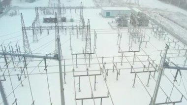 Electrical grid substation and high voltage electric switchyard converter transformer in America at winter snow storm. Power station with pylons and distribution cables for EV charging stations.