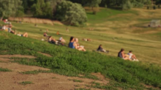 トロントの公園にある太陽の下で芝生の上でリラックスしているカナダ人の背景をぼんやりと 夏にリバーデール公園でスポーツゲームをしている人々 — ストック動画