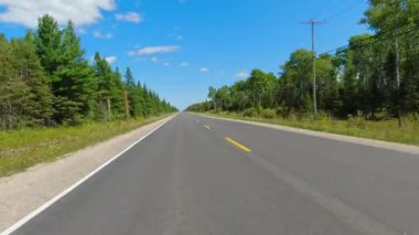 Geriye dönük sürücü plakası geriye doğru bakıyor. POV araba manzaralı. 540 numaralı otoyol, düz yol. Manitoulin Adası, Ontario, Kanada 28 Ağustos 2023 Orman, çiftlikler ve çayırlık arazi.