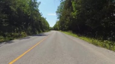 Ön manzara otoyolda plaka kullanıyordu. POV araba manzaralı. Ağaçlık ormanı olan kırsal dolambaçlı bir yol. Güneşli öğleden sonra mavi gökyüzü. Manitoulin Adası 'nda virajlı yol.