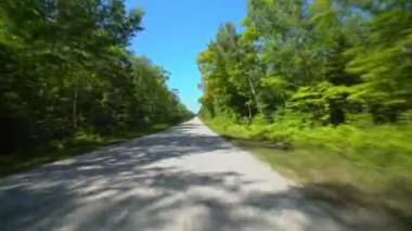 Çarpışan off road, orman yolu boyunca sürerken dublörlük yapıyor. Ön manzara sürücü plakası ileriye bakıyor. POV araba manzaralı. Kırsal düz yolda açık mavi gökyüzü. İleride araba yok..