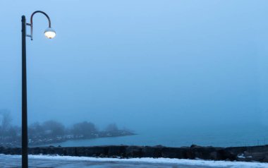 Gölde yağışlı sisli hava. Su kıyısında ve ağaçlarda sisli bir sis esiyor. Soğuk sisli yağmurlu kış akşamı. Scarborough Kayalıkları ya da Kayalıklar Ontario göl suları. 