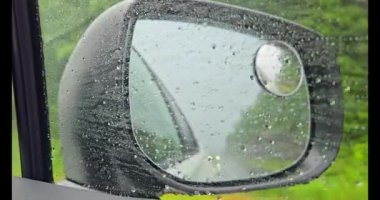 Sonbaharda bulutlu yağmurlu bir havada otoyolda giden bir arabanın yan aynası. Aracın süratinden dolayı vitrindeki hızlı damlalara yakın çekim. Damlayan yağmur damlaları.