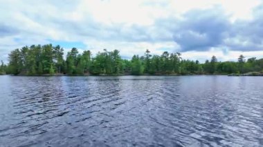 Güzel köknar ağaçları ve teknede balık avlarken gölün kayalık kıyı şeridi manzarası. Hobilerin yaşam tarzı balıkçılık. Eğlence amaçlı balık tutma sporu. Şaşırtıcı Kuzey Amerika doğası.