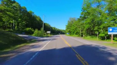 28. otoban kayalık yeşillikten geçiyor. Uzun yeşil ormanlar boyunca asfalt yol. Arabanın arka kısmından sürüş plakası: Bancroft, Kawartha, Ontario, Kanada - 28 Haziran 2024