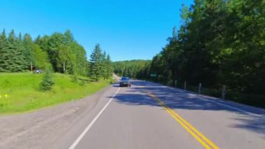 Bagajın arka tarafındaki geniş arabanın sürücü plakası. Arka ya da beşinci kapı pencere manzaralı. Düz asfalt yol POV Karayolu 28: Bancroft, Kawartha, Ontario, Kanada - 28 Haziran 2024