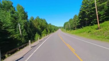 28. otobanın geniş açılı çekim plakalı kamera pov 'u Kanada kalkanının yeşillik bolluğunu geçiyor. Arabanın arkasından asfalt yol manzarası: Bancroft, Kawartha, Ontario, Kanada - 28 Haziran 2024