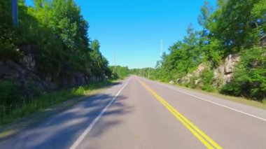 POV 28. karayolunu kullanarak Bancroft ve Kawartha, Ontario, Kanada arasındaki kayalık yeşilliği geçiyor. Uzun yeşil ormanlar boyunca asfalt yol. Arabanın arka koltuğundan sürüş plakası.