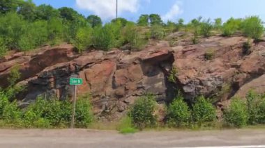 Bakış açısı, sağ taraf araba manzarası. Yolcu vitrinli araç manzaralı, POV 'lu 11. Otoyol' da. Kaya duvarları ve yeşil ağaçları olan Kanada yolları. Kanada Kalkanı. Araba filmi desteği