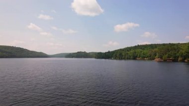 Yeşil orman ve tatil kulübeleriyle çevrili Baptist Gölü 'nün alçak drone manzarası, Kanada' da dağınık bulutlu mavi gökyüzü. Bancroft yakınlarında Kuzey Ontario 'nun temiz suları.