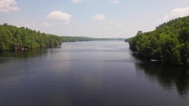Yeşil orman ve tatil kulübeleriyle çevrili Baptist Gölü 'nün alçak drone manzarası, Kanada' da dağınık bulutlu mavi gökyüzü. Bancroft yakınlarında Kuzey Ontario 'nun temiz suları.