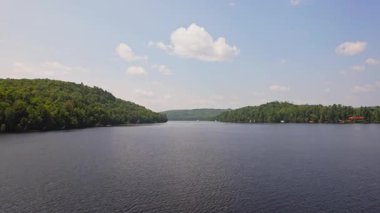 Yeşil orman ve tatil kulübeleriyle çevrili Baptist Gölü 'nün alçak drone manzarası, Kanada' da dağınık bulutlu mavi gökyüzü. Bancroft yakınlarında Kuzey Ontario 'nun temiz suları.