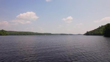 Yeşil orman ve tatil kulübeleriyle çevrili Baptist Gölü 'nün alçak drone manzarası, Kanada' da dağınık bulutlu mavi gökyüzü. Bancroft yakınlarında Kuzey Ontario 'nun temiz suları.