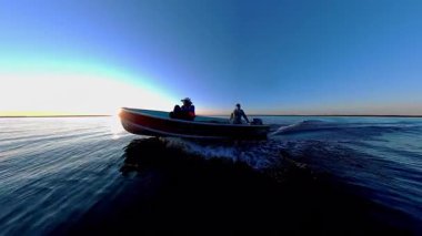 Kara siluetiyle altın saat batımında süzülen balıkçı tekneleriyle turistler. Balık tutmak için en iyi zaman. Tekneden güneşin battığı göl manzarası. Akşam eğlencesinin sinematik görüntüsü.