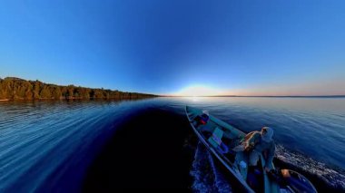 Kara siluetiyle altın saat batımında süzülen balıkçı tekneleriyle turistler. Balık tutmak için en iyi zaman. Tekneden güneşin battığı göl manzarası. Akşam eğlencesinin sinematik görüntüsü.