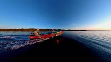 Kara siluetiyle altın saat batımında süzülen balıkçı tekneleriyle turistler. Balık tutmak için en iyi zaman. Tekneden güneşin battığı göl manzarası. Akşam eğlencesinin sinematik görüntüsü.