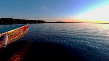 Gün batımında kara siluetiyle sakin suda süzülen tekne pruvası. Balık tutmak için en iyi zaman. Tekneden göl manzarası. Akşam eğlencesinin sinematik görüntüsü.