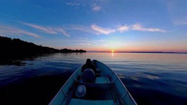 Kara siluetiyle altın saat batımında süzülen balıkçı tekneleriyle turistler. Balık tutmak için en iyi zaman. Tekneden güneşin battığı göl manzarası. Akşam eğlencesinin sinematik görüntüsü.