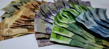 Stacks of Indonesian banknotes of various denominations and colors, isolated on white background.