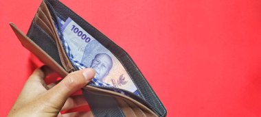 A man holding a wallet containing new Indonesian banknotes issued in 2022. Rupiah currency concept isolated on a red background. Negative space