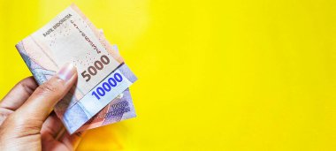 A man holding new Indonesian banknotes issued in 2022. Rupiah currency concept isolated on a yellow background. Negative space