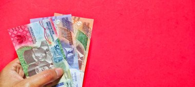 Man holding new Indonesian banknotes issued in 2022. Rupiah currency concept isolated on a red background. Negative space