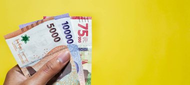 A man holding new Indonesian banknotes issued in 2022. Rupiah currency concept isolated on a yellow background. Top view