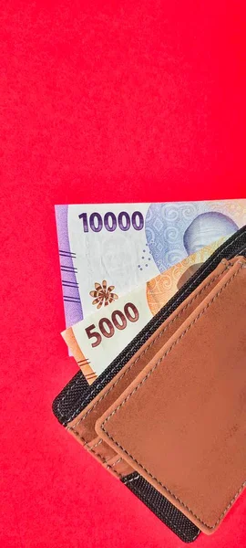 Portrait of a wallet containing new Indonesian banknotes issued in 2022. Rupiah currency concept isolated on red background