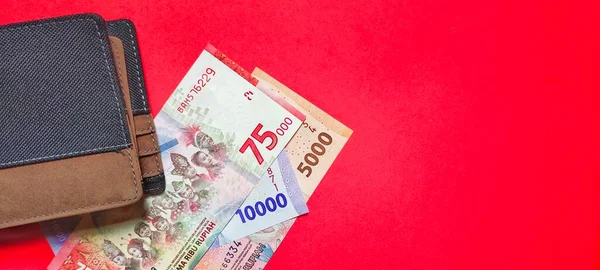 Top view of a wallet and new Indonesian rupiah banknotes issued in 2022. Rupiah currency concept isolated on red background. Negative space