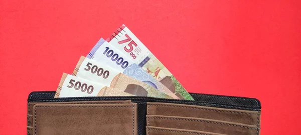 İçinde 2022 'de yayınlanan yeni Endonezya banknotlarının bulunduğu cüzdanın üst görüntüsü. Kırmızı arkaplanda izole edilmiş rupiah para birimi kavramı