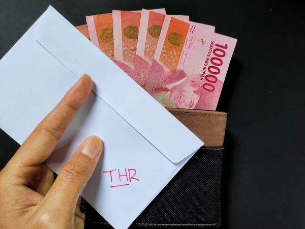 THR ve yeni Endonezya banknotlarından oluşan beyaz bir zarf tutan adam, genellikle Tunjangan Hari Raya veya THR adı verilen banknotlar bayram öncesinde çalışanlara veriliyor..