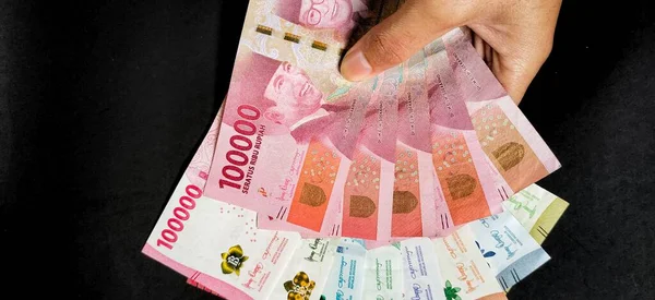 2022 'de çıkarılan yeni Endonezya banknotlarını elinde tutan bir adamın üst görüntüsü. Rupiah para birimi kavramı siyah arkaplanda izole edildi.
