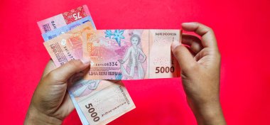 Bir adam 2022 'de çıkarılan yeni Endonezya banknotlarını elinde tutuyor. Kırmızı arkaplanda izole edilmiş yeni rupiah para birimi kavramı. 