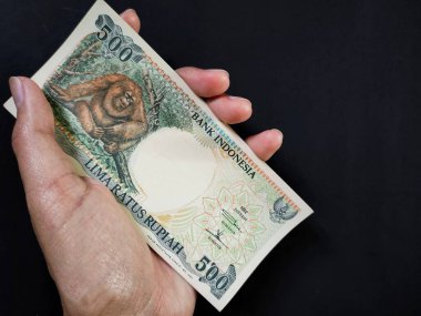 1992 'de çıkarılmış 500 rupilik Endonezya banknotları elinde tutan adam. Eski rupiah para birimi kavramı siyah arka planda izole