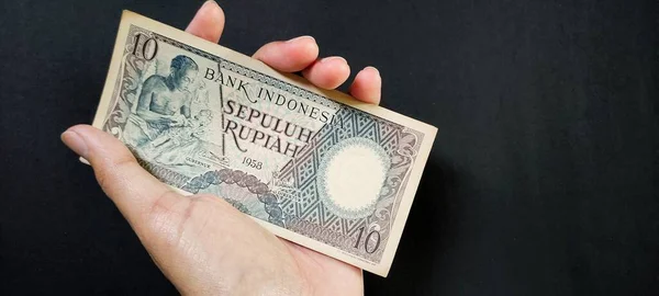 1963 'te yayınlanan eski Endonezya banknotları Rp.10 rupiah' ı elinde tutan bir adam. Siyah arka planda izole edilmiş eski rupiah para birimi kavramı. Üst görünüm