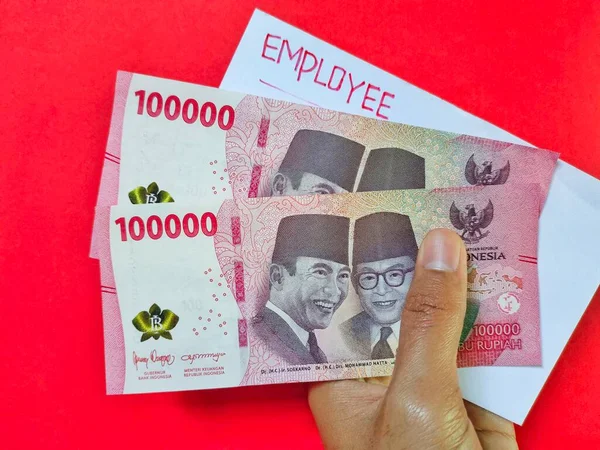 EMPLOYEE ve yeni Endonezya banknotlarından oluşan beyaz bir zarf tutan adam. Genellikle, çalışanların maaşları üzerinde 