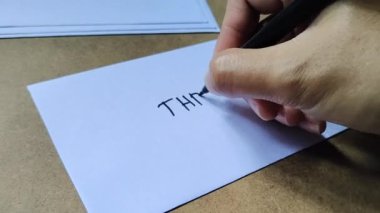 Kahverengi ahşap arka planda beyaz zarfa üç harfli yazı yazan adam. Bu zarf, bayramdan önce çalışanlara verilen izinleri içerir..