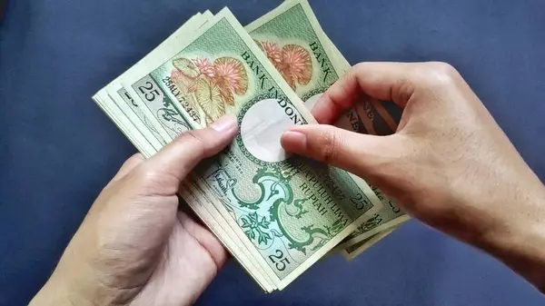 Siyah arka planda izole edilmiş Rp 25 rupiah banknotları sayan bir adamın üst görüntüsü..