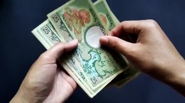 25 Rupi 'lik eski rupiah banknotlarını sayan bir erkek. Siyah bir arka planda izole edilmiş..