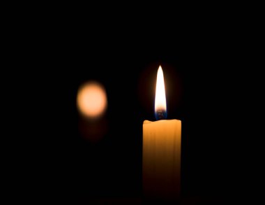 Karanlıkta yanan bir mum ışığı ve karanlık bir arka planda parlayan bir ışık.