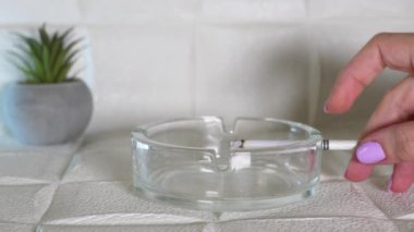 Bir kadının eli, sigaradan çıkan dumanlı bir sigarayı kül tablasına koydu. Sigara içmenin zararı. Sağlıklı bir yaşam tarzı. 4K yatay video.