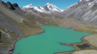 Turkuaz alp gölü karla kaplı dağlarla çevrili, hava aracı perspektifinden çekilmiş.
