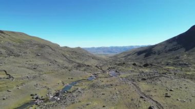 Açık mavi gökyüzünün altında nehir olan bir dağ vadisinin havadan görünüşü doğanın güzelliğini vurguluyor.