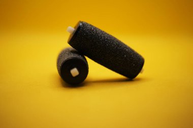 Rengarenk iki siyah sünger silindiri, altlarında canlı sarı bir yüzey üzerinde üst üste düzgünce ve dikkatlice istiflenmiştir.