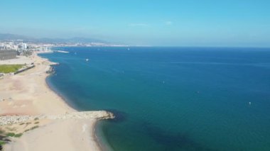 Bu hava görüntüleri, berrak bir gökyüzünün altında parıldayan okyanusla ve kumlu kıyı şeridinin üzerinde bir şehrin ufuk çizgisi ile tamamlanmış sıcak bir parıltıyla nefes kesici bir sahili yakalıyor.