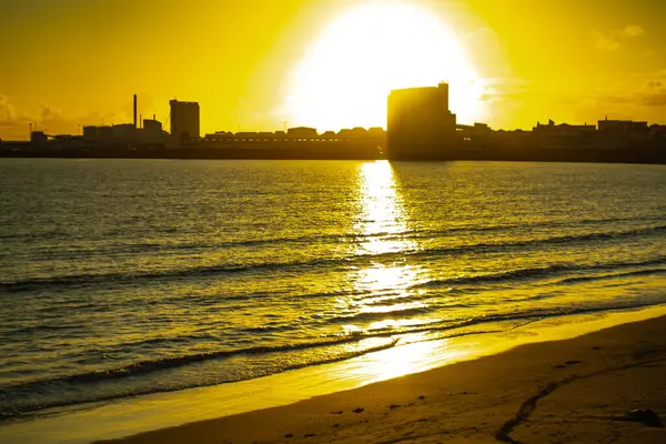 Plaj ve deniz yansımaları ile kentsel kıyı şeridi üzerinde altın gün batımı
