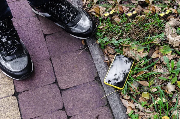 Smartphone with a broken display lies at the feet of a person on the asphalt