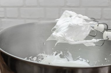 Meringue için çırpılmış yumurta beyazı ve şeker karıştırma kabında elektrikli el çırpma ile karıştırılmış. Mutfak aletleri ile aşçılık süreci.