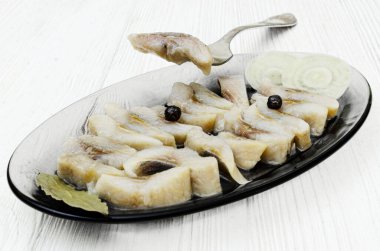 Yakın plan. Soğan dilimleri ve karabiberlerle süslenmiş düzgünce düzenlenmiş ringa balığı dilimleriyle dolu bir bardak servis tabağı..